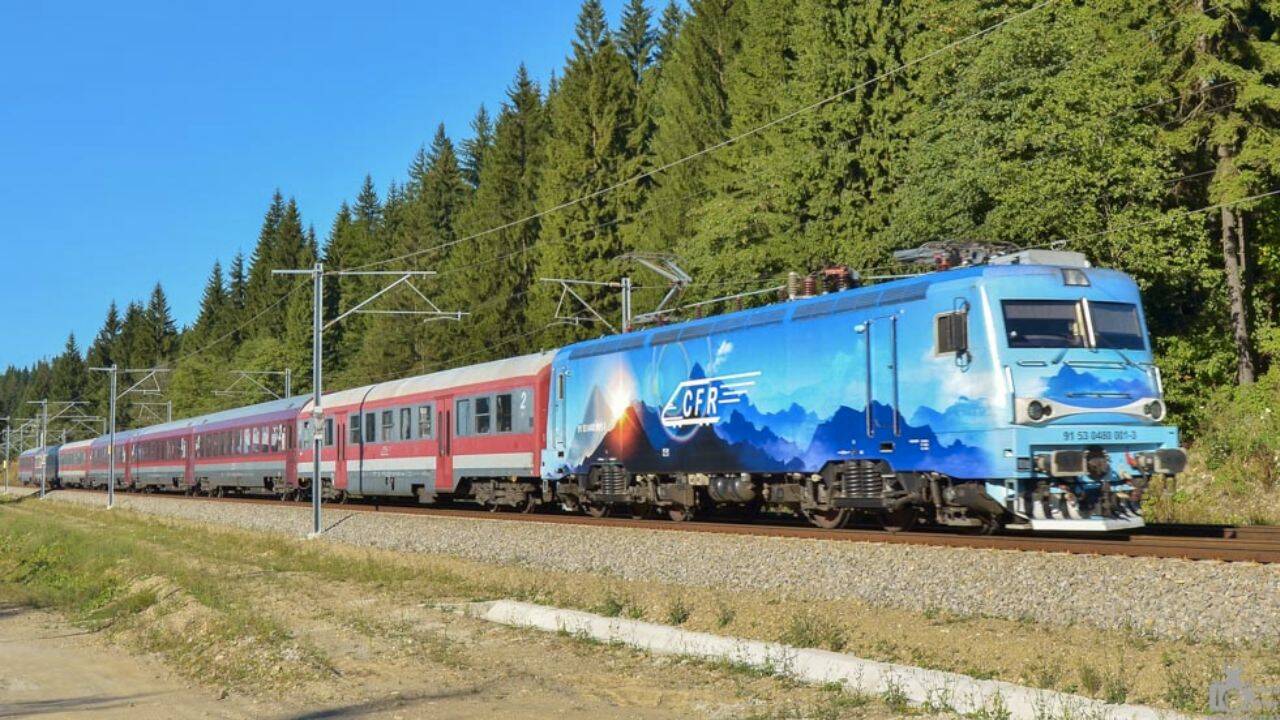 un tren care se deplaseaza pe langa o padure