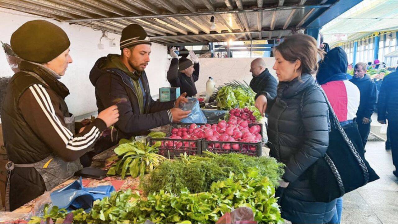 mai multe persoane in jurul unei tarabe cu legume