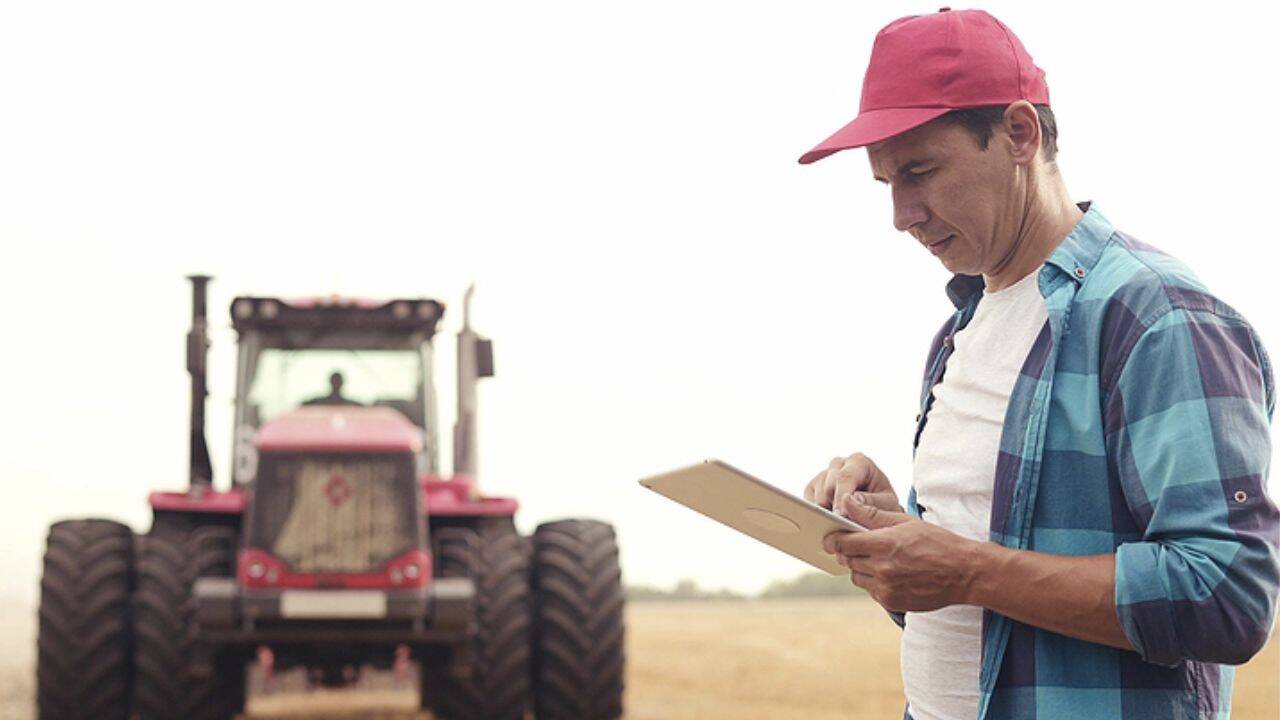 o persoana care verifica o tableta si un tractor pe fundal